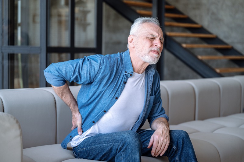 Person holding lower back on sofa in Clayton Heights Surrey Langley